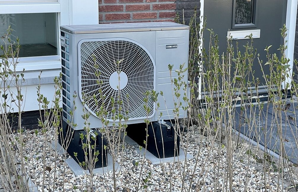 Außengerät einer Luft-Wärmepumpe auf einer Schottereinfassung nebem einem Gebäude.
